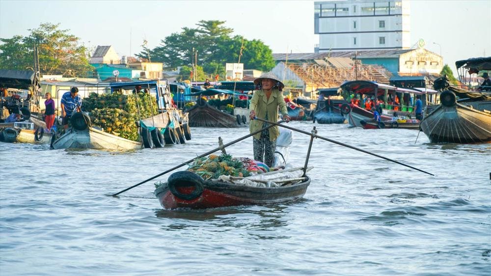 A vendor rows her boat through a vibrant floating market in the Mekong Delta during the rainy season